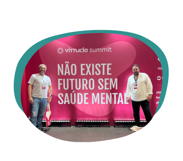 Sócios Alex Camargo e Tiago Gusmão posando no painel do evento Vittude Summit, em frente a um letreiro que diz: Não existe futuro sem saúde mental