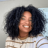 Foto de rosto de Isabela sorrindo, com cabelos cacheados volumosos e blusa listrada